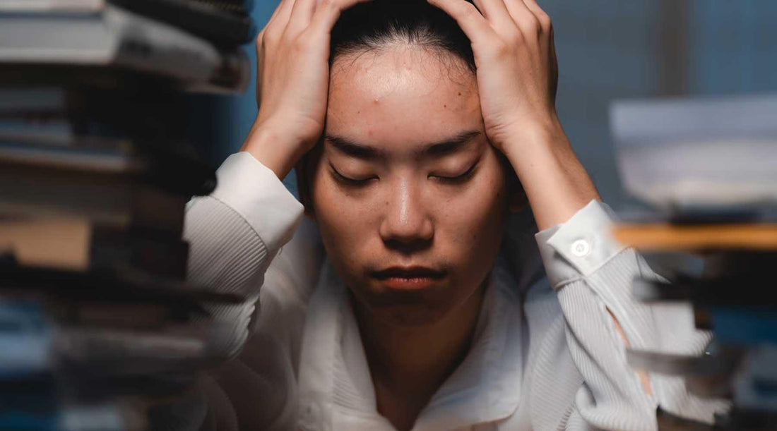 Persona con estrés, rodeada de libros, simbolizando agotamiento mental y búsqueda de bienestar