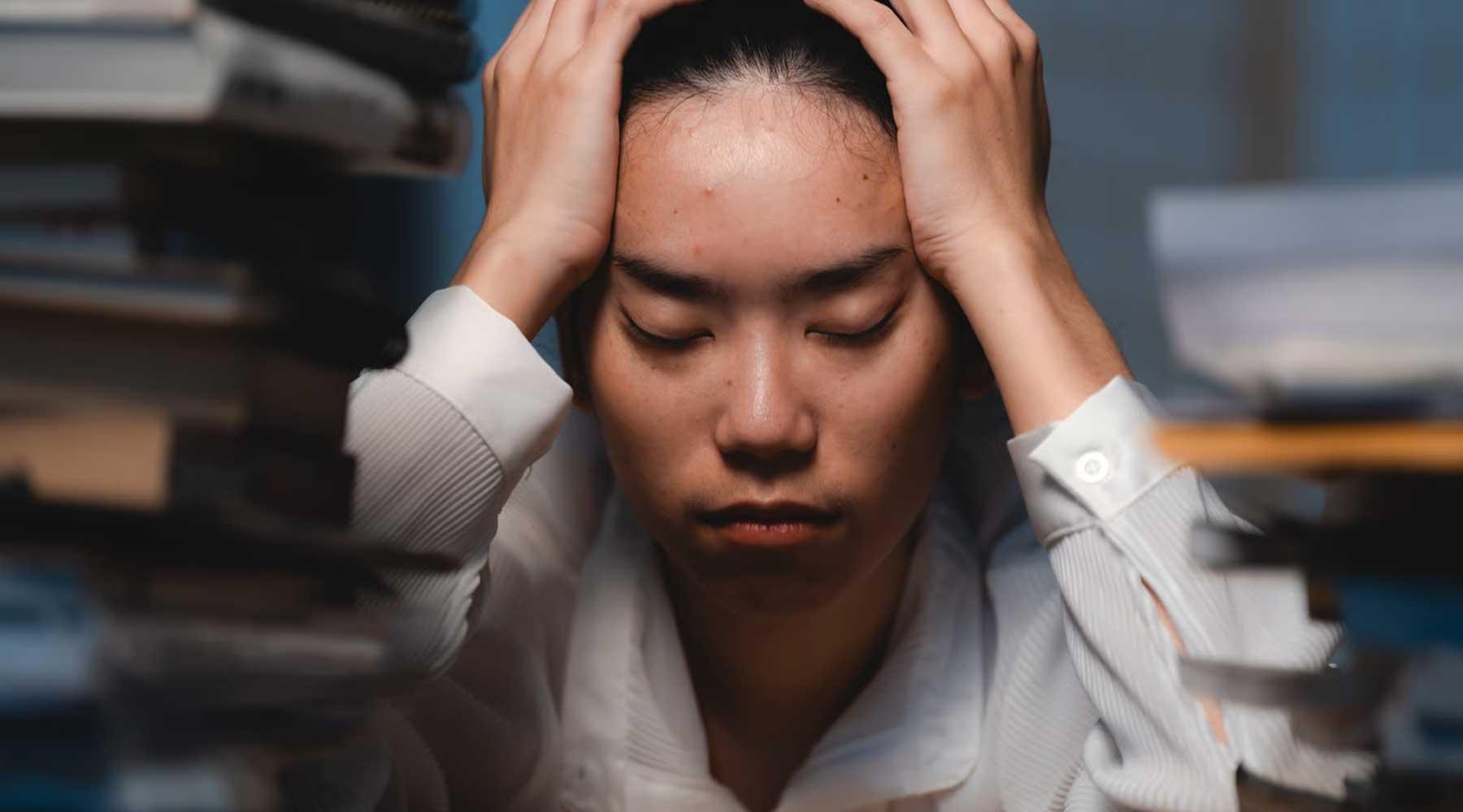 Persona con estrés, rodeada de libros, simbolizando agotamiento mental y búsqueda de bienestar