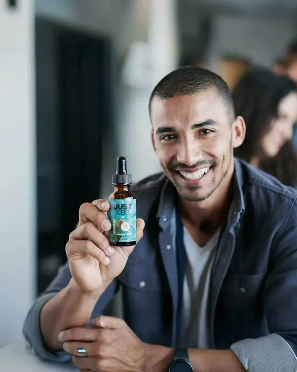 Hombre sonriendo sostiene frasco de aceite JustCBD, bienestar y productos CBD Sensus.Life