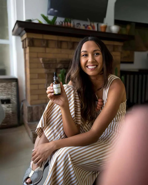 Mujer sonriente con vestido de rayas sostiene gotero Sensus Lions Mane en sala hogareña, bienestar